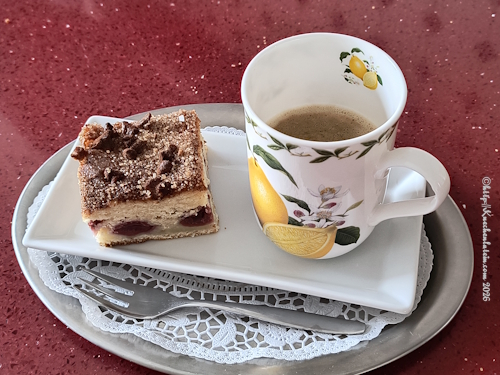 Ein quadratisches Stück Kaffeekuchen mit Kirschen neben einer Tasse Kaffee