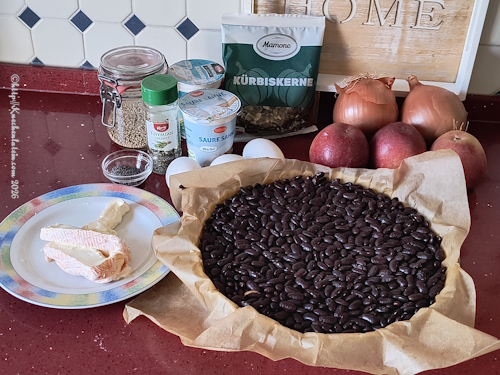 Einzelzutaten für Apfel-Zwiebel-Quiche mit Mohn auf Arbeitsfläche