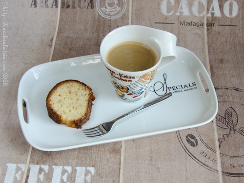 Ein Stück Miami-Beach-Sauerrahmkuchen mit feiner Krume auf einem Teller, daneben eine Tasse Kaffee