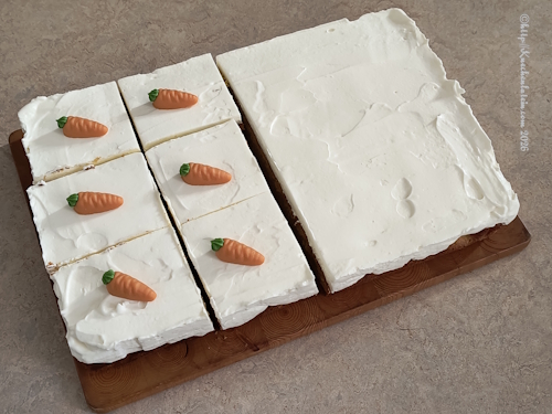 Schwedischer Karottenkuchen Morotsrutor mit Frosting auf einem Backblech auf einem Blech teilweise schon in Quadrate geschnitten und mit Marzipanrübe dekoriert