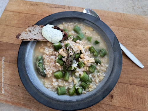 Ein Teller angerichtete Spargelsuppe mit Graupen und gelben Erbsen mit einer Scheibe Brot und Petersiliencreme garniert