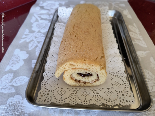 Glutenfreie Mandelrolle mit Haselnusscremefüllung, serviert auf weißem Spitzenpapier auf einem glänzenden Edelstahltablett.