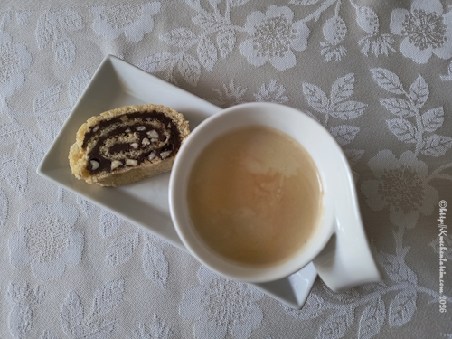 Eine Scheibe Mandelrolle mit Haselnusscreme neben einer Tasse Kaffee auf einem Porzellantablett