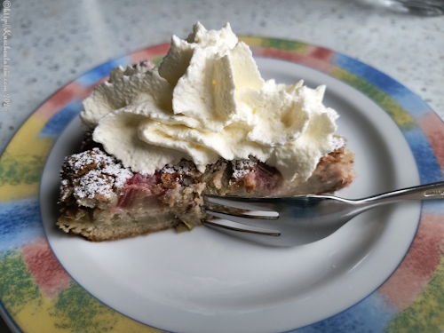 1 Stück Rhabarber-Kladdkaka mit weißer Schokolade und Kardamom auf Teller mit Sahne angerichtet