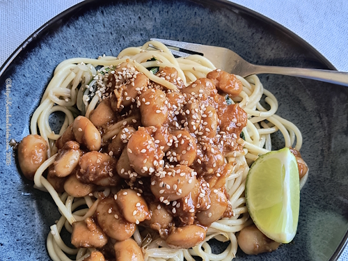 Pasta mit karamellisierten Bohnen und Spinat auf Teller mit Gabel und Limettenviertel angerichtet